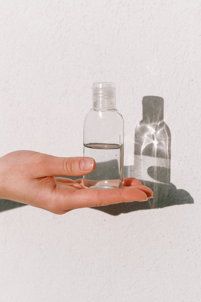 A hand holding a clear sanitizer bottle against a white background, emphasizing cleanliness.
