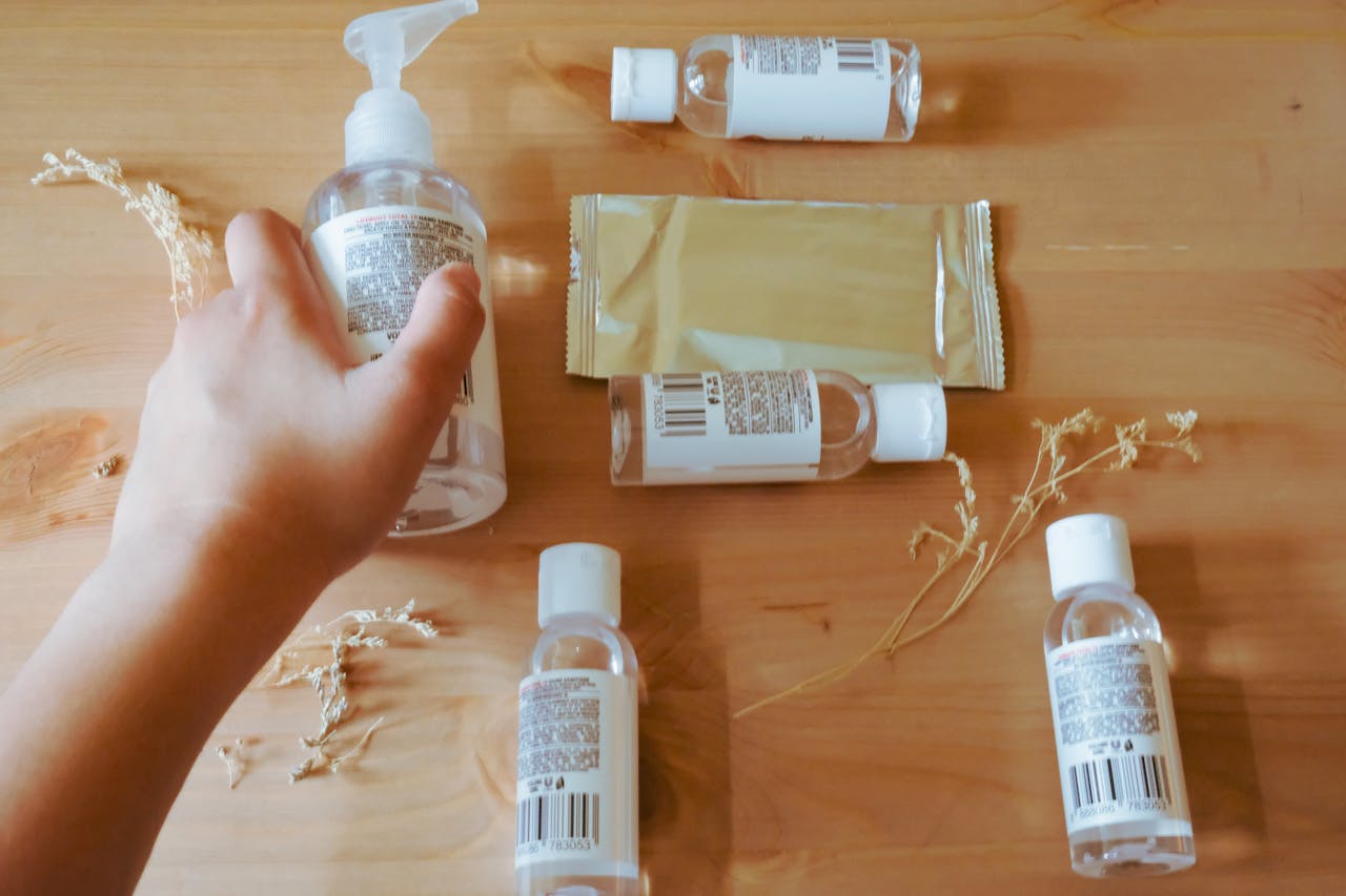 A hand reaching for a sanitizer bottle among wipes and other bottles on a wooden table.