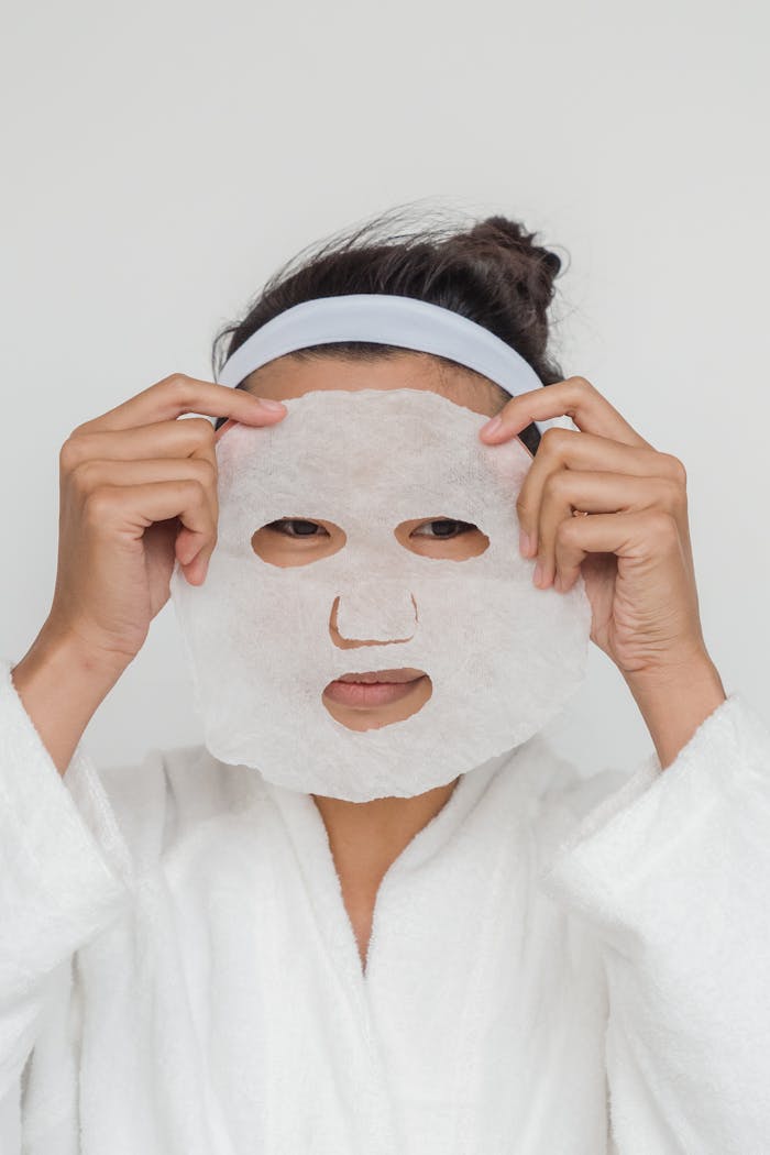 Adult woman applying a facial sheet mask in a skincare routine indoors.